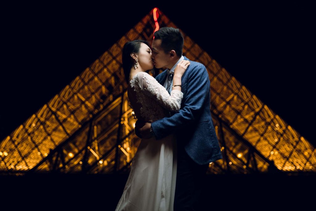 le marié embrasse la mariée devant les pyramides du Louvre